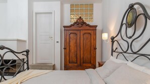 Un dormitorio con cama, armario, ventana y lámpara fijada a la pared.