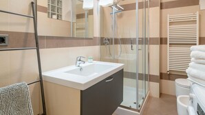 Un baño moderno con cabina de ducha de vidrio, un lavamanos blanco y un perchero para toallas.