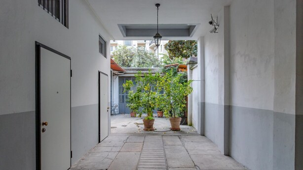 Un pasillo estrecho con suelo de baldosas, una puerta a la izquierda y plantas en macetas a la derecha.