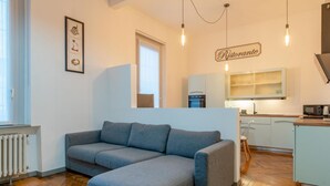 Una sala de estar moderna con un sofá gris, un radiador, un cuadro enmarcado y una zona de cocina con un letrero que dice "Ristorante".