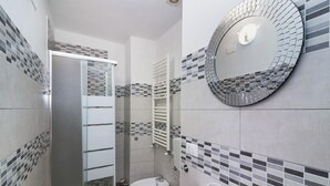 Une salle de bain moderne avec une douche à parois de verre, un miroir rond, un lavabo avec un robinet et des toilettes.