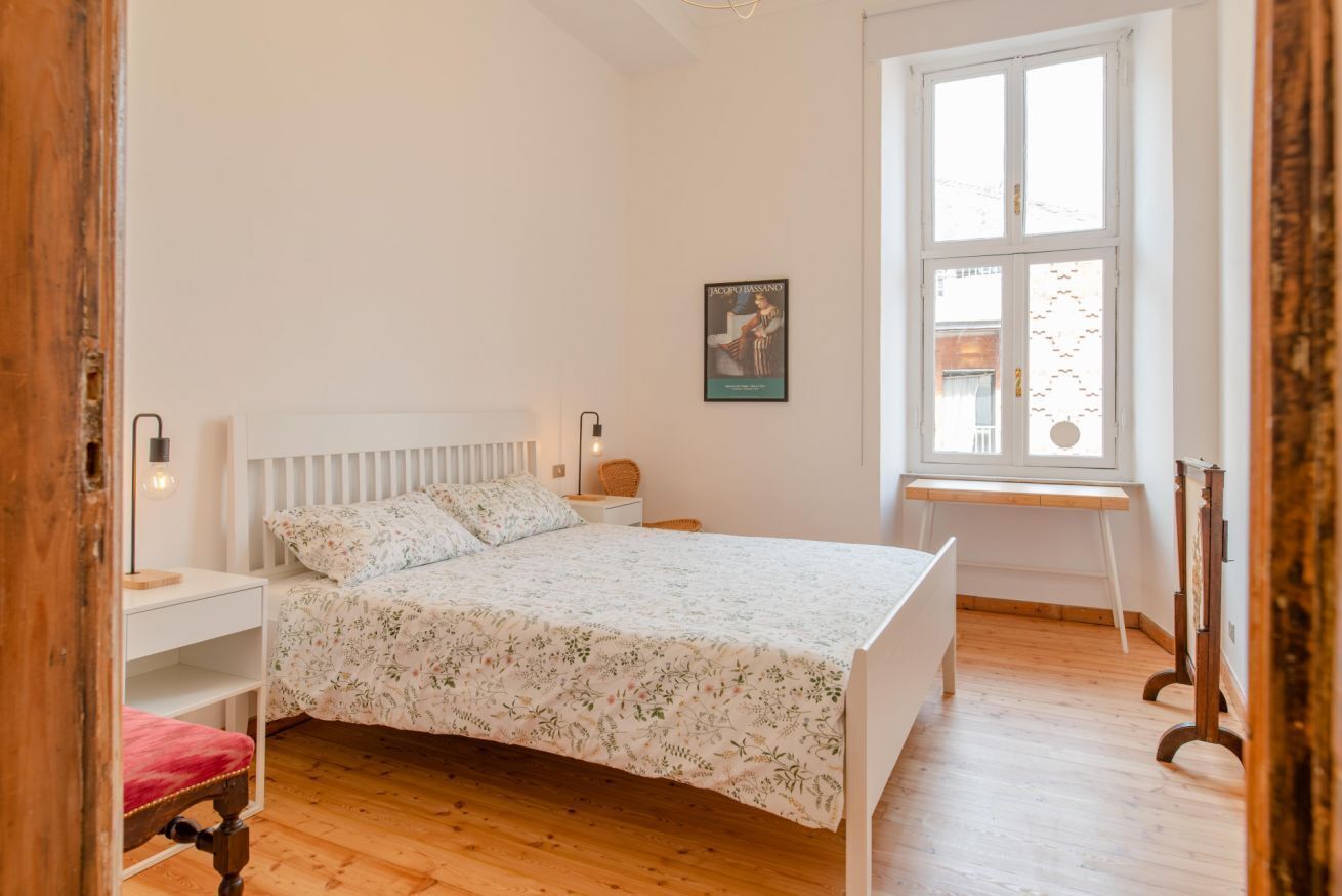 A bedroom with a bed, a desk, and a window.
