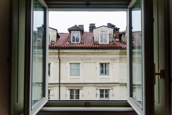 A view through an open window of a building with multiple stories, featuring a red-tiled roof and white walls. - Palatium by HappyHosTorino (Torino)