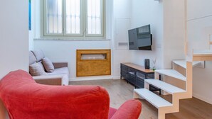 A modern living room with a red chair, a grey sofa, a wooden cabinet, a TV mounted on the wall, and a staircase. - [Centro]: Dream Loft by HappyHosTorino (Torino)