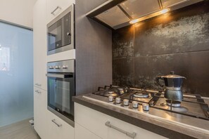 A modern kitchen with a built-in oven, a stovetop with a coffee pot, and a microwave.