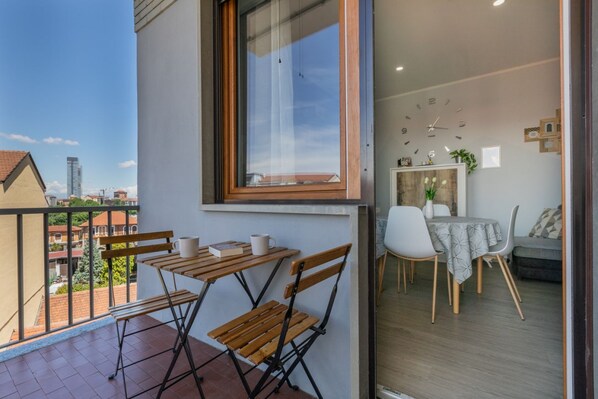 A balcony with a table and chairs, a dining area with a clock, and a view of buildings.