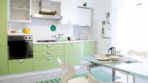 Une cuisine moderne avec des meubles de couleur verte, une cuisinière à gaz et un coin repas comprenant une table et des chaises en verre.