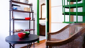 Une pièce comprenant une chaise en bois, une table ronde avec un bol rouge et vert, et une bibliothèque en bois contenant divers objets.