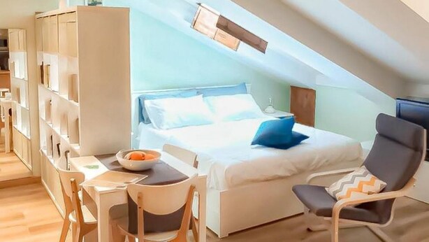 A bedroom with a bed, bedside table, and a chair. There is a desk with a chair and a bookshelf.