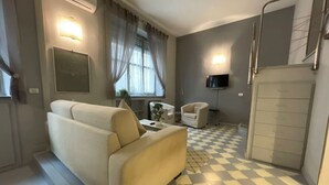 Una sala de estar moderna con un sofá, una pequeña mesa con una planta y un televisor montado en la pared.