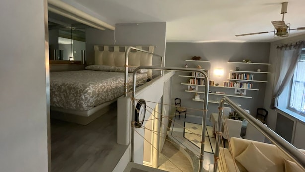 Un dormitorio moderno con cama elevada, una escalera y una zona de lectura con estanterías.