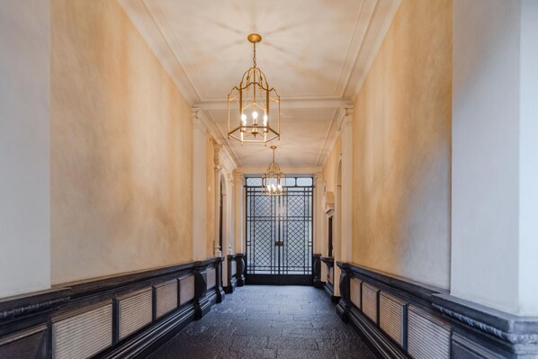 A hallway with a black and white marble floor, a black balustrade, and a large, ornate gate at the end.