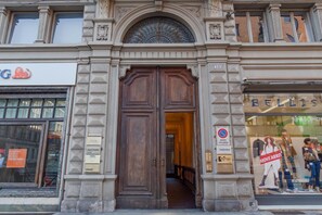 A building with a large wooden double door, a sign for 'BELLIS' on the right, and a 'no parking' sign on the left.