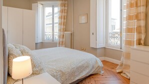 A bedroom with a bed, a bedside table with a lamp, a window with curtains, and a radiator. - Enjoy Torino City Center (Torino)