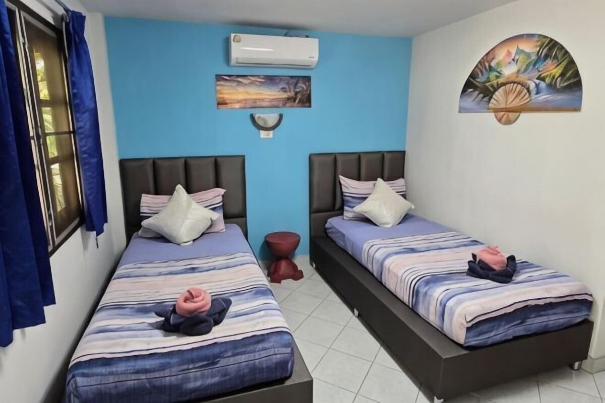 A room with two beds, a window with curtains, an air conditioning unit, and a wall-mounted artwork.