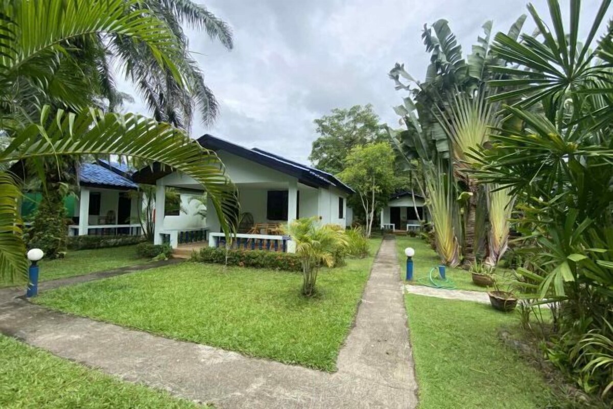 A bungalow with a covered porch, surrounded by lush tropical vegetation.
