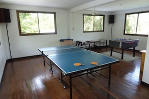 A room with a ping pong table, a foosball table, and a window with a view of greenery. - Sabai Resort (Krabi)