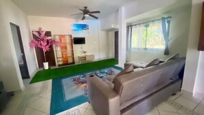 Un salon avec un canapé, un ventilateur de plafond, un téléviseur et une fenêtre avec des rideaux.