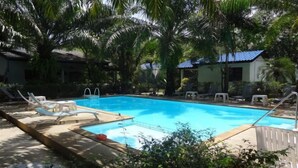 Une piscine avec des chaises longues et un petit bâtiment avec un toit bleu en arrière-plan.