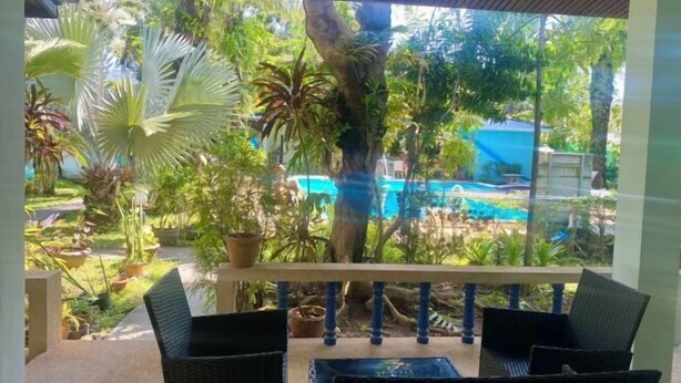 Un espace extérieur aménagé avec des meubles en osier, abrité et offrant une vue sur une piscine, ainsi qu’une végétation luxuriante.