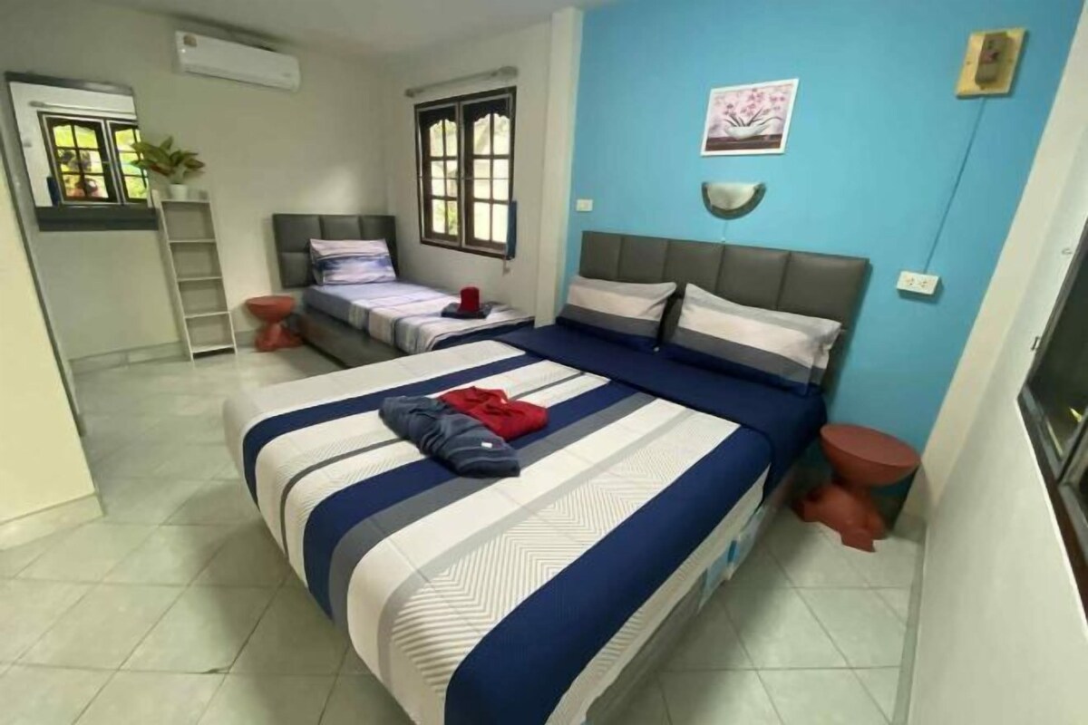 A bedroom with a large bed, two smaller beds, a window, a wall-mounted shelf, and a small stool.