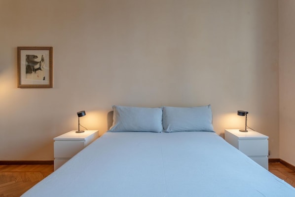 Ein Schlafzimmer mit einem großen Bett, zwei Nachttischen und einem gerahmten Bild an der Wand.