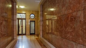 A hallway with marble walls and a polished floor, leading to a door with a circular mirror above it.