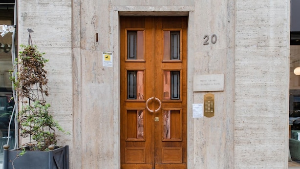 A double wooden door with a brass knocker, a number plaque, and a small sign on the wall.