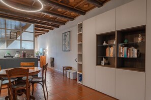 A modern kitchen with wooden beams, a dining area with a round table and chairs, and a bookshelf with books and decorative items. - Casa Mimmo by Happyhostorino (Turin)