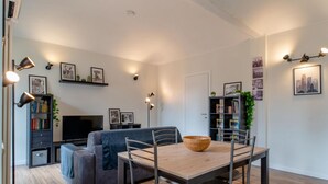 Un salon moderne avec un canapé, une table à manger et des chaises. On y trouve également des étagères, un téléviseur et des lampes fixées au mur.