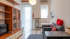 A modern living room with a wooden cabinet, a grey sofa with red cushions, a television, and a hanging light fixture. - Perrero4 by Happyhostorino (Torino)
