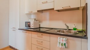 A kitchen with white cabinets, a black countertop, a microwave, a sink, and a green soap dispenser.