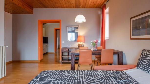 A room with a wooden ceiling, a bed with a zebra print bedspread, a dining table with chairs, a lamp, and a framed picture on the wall.