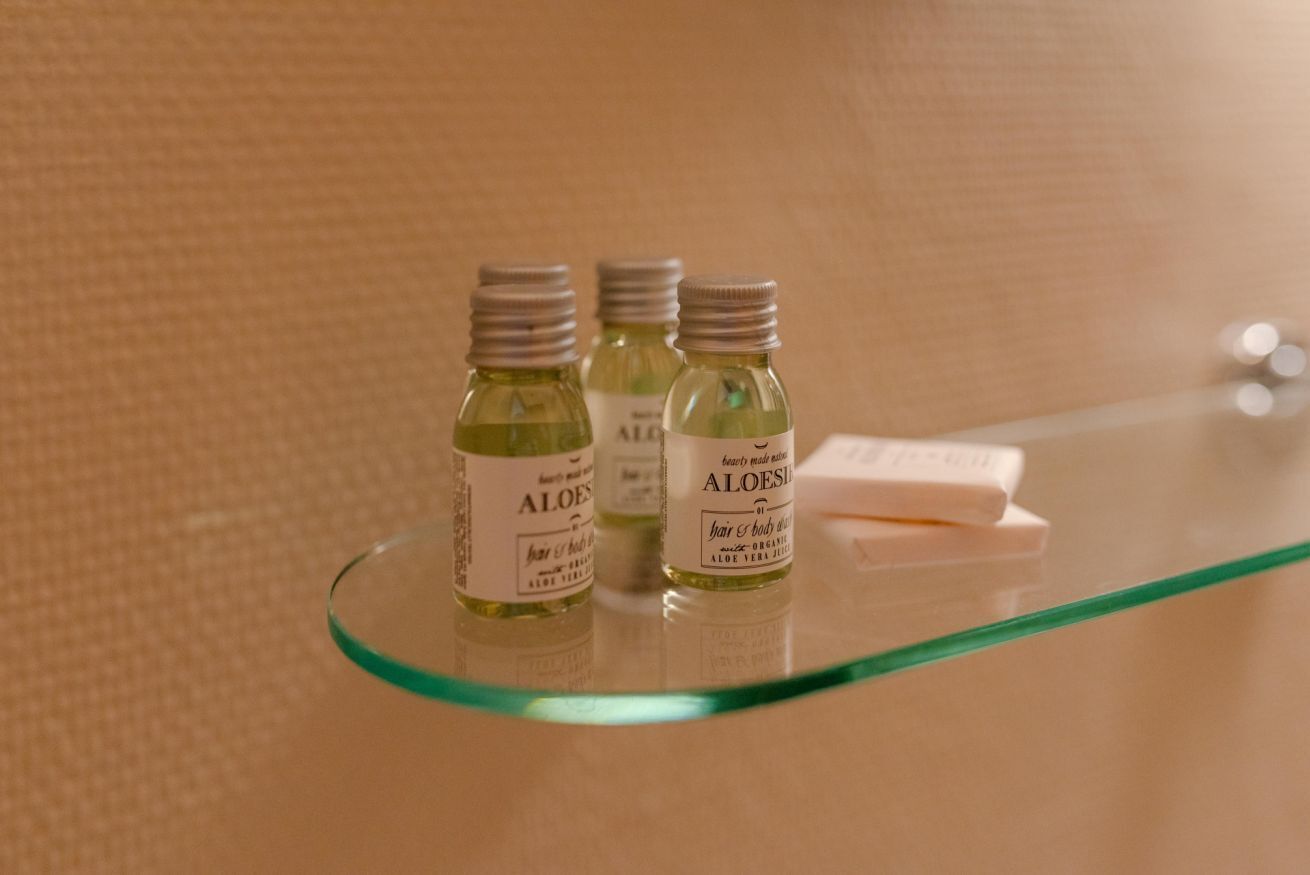 Trois petits flacons de gel d’aloe vera sont posés sur une étagère en verre, à côté d’un savon.