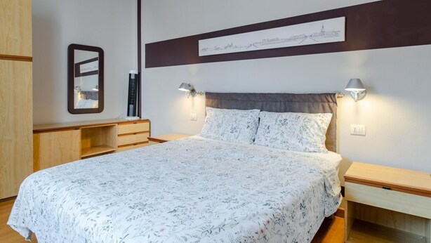 A bedroom with a large bed, two bedside tables, a nightstand, a wardrobe, and a wall-mounted artwork. - San Domenico_222 by Happyhostorino (Torino)