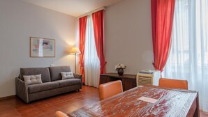 A furnished living room with a sofa, dining table, and chairs, a lamp, and a radiator. - San Domenico_222 by Happyhostorino (Torino)