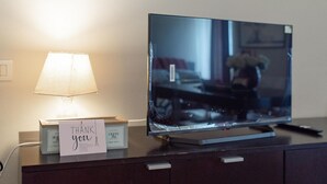 A television on a dark wooden dresser with a lamp and a thank you card.