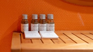 Four bottles of ALOEISIR on a wooden bench against an orange textured wall.