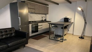 A modern kitchen with a refrigerator, stove, and microwave. There's a bar stool and a floor lamp.