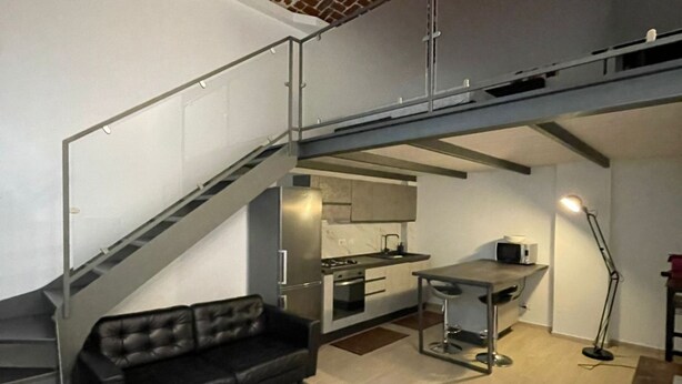 A modern kitchen with stainless steel appliances, a dining area with a table and chairs, and a black leather sofa.