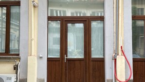 A building facade with a brown wooden door, beige pillars, and a red hose attached to a beige pipe.