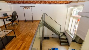 A modern office space with a wooden floor, a glass railing, a desk with a chair, and a staircase.