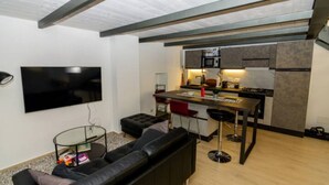 A compact living space with a modern kitchen, a flat-screen TV, a sofa, and a dining area with stools.