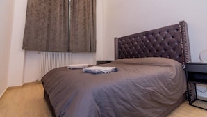 A bedroom with a large bed, a tufted headboard, a radiator, and a window with curtains.