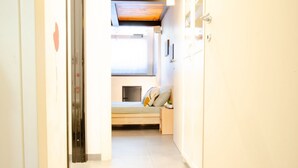 Un estrecho pasillo que conduce a un dormitorio con una cama, una mesita de noche pequeña y una ventana.