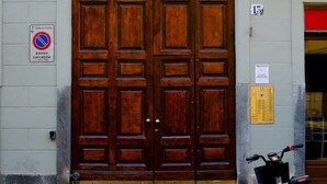 Una gran puerta doble de madera con un picaporte metálico, un letrero de no estacionamiento y una placa con el número de la puerta.
