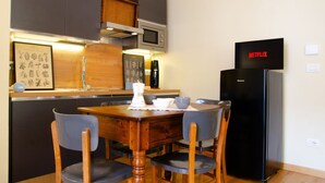 A compact kitchen with a wooden dining table, chairs, a black refrigerator, a microwave, and a Netflix sign. - [Zona Borgo Dora] La Terrazza by HappyHosTorino (Torino)