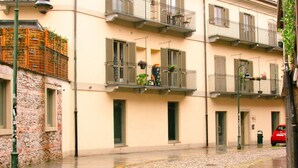 A street with a building featuring balconies with plants, a stone wall, and a red car parked on the side. - [Zona Borgo Dora] La Terrazza by HappyHosTorino (Torino)