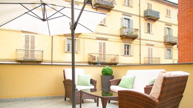 A balcony with wicker furniture, a glass table, and a potted plant. - [Zona Borgo Dora] La Terrazza by HappyHosTorino (Torino)