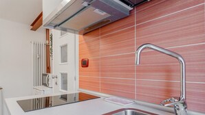 Een moderne keuken met een roestvrijstalen spoelbak, een inbouwoven en een rode tegelachtergrond.
